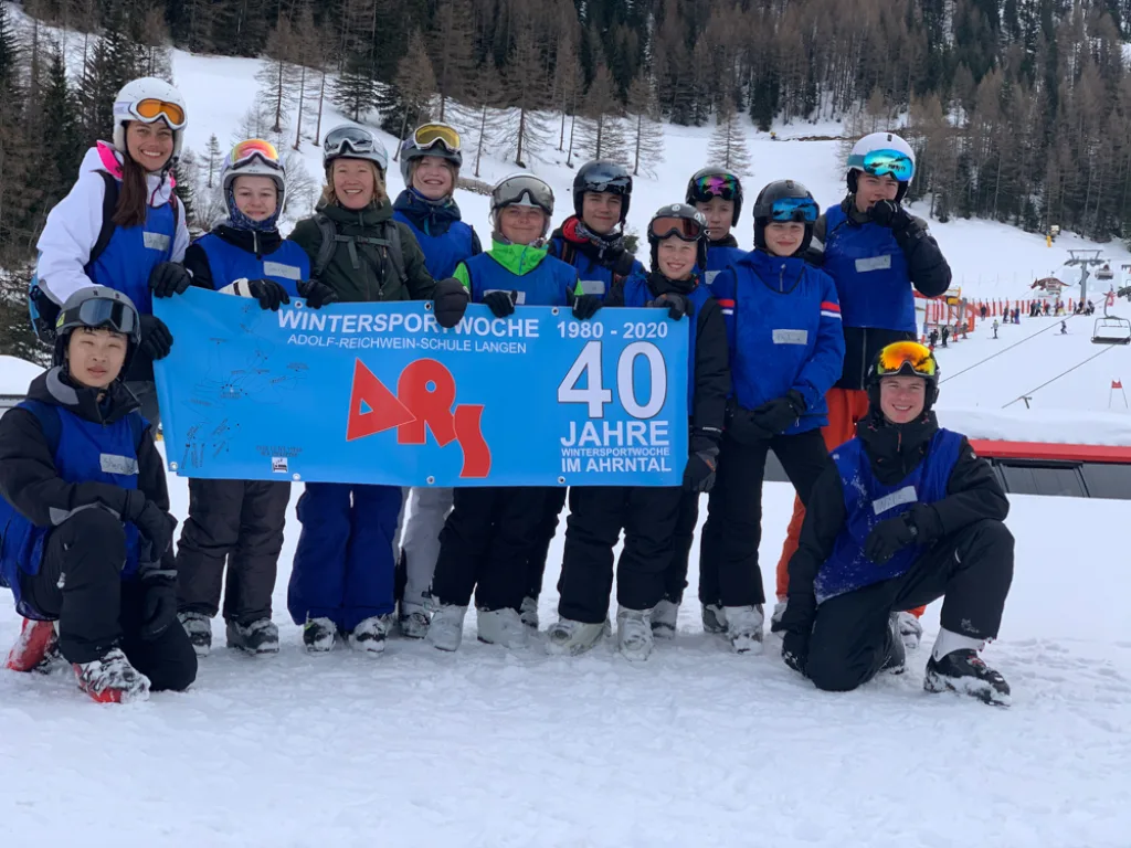 Jugendliche mit Helm und Skibrille halten das Jubiläumsbanner der Wintersportwoche.